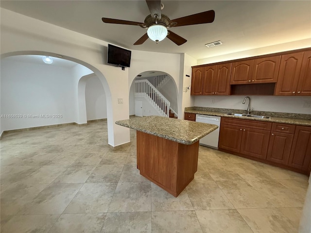 kitchen featuring ceiling fan, dishwasher, light stone counters, and sink