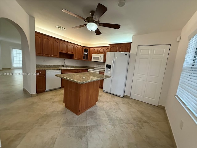 kitchen with ceiling fan, sink, dark stone countertops, white appliances, and a kitchen island