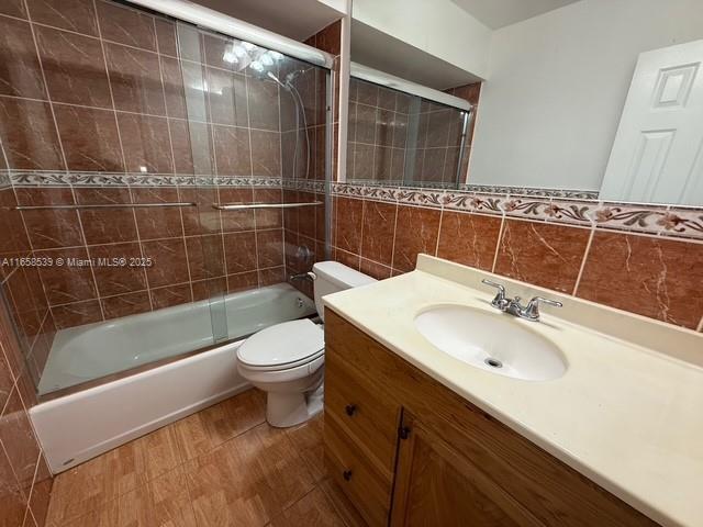 full bathroom with vanity, combined bath / shower with glass door, decorative backsplash, toilet, and tile walls