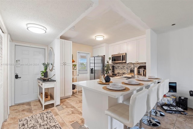 kitchen with white cabinetry, a textured ceiling, a kitchen bar, tasteful backsplash, and appliances with stainless steel finishes