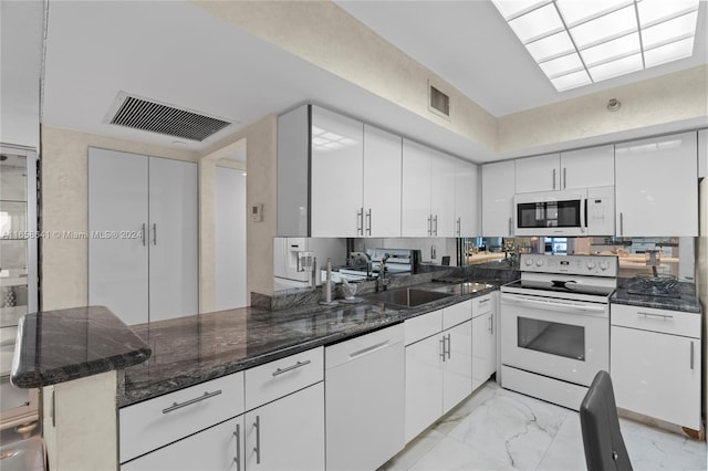 kitchen with white cabinets, sink, kitchen peninsula, white appliances, and a breakfast bar area