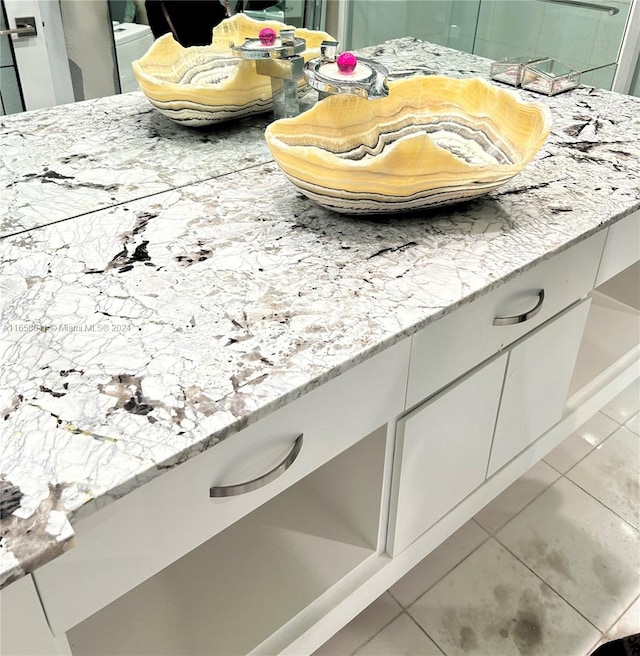 interior details featuring light stone counters, white cabinets, and tile patterned flooring