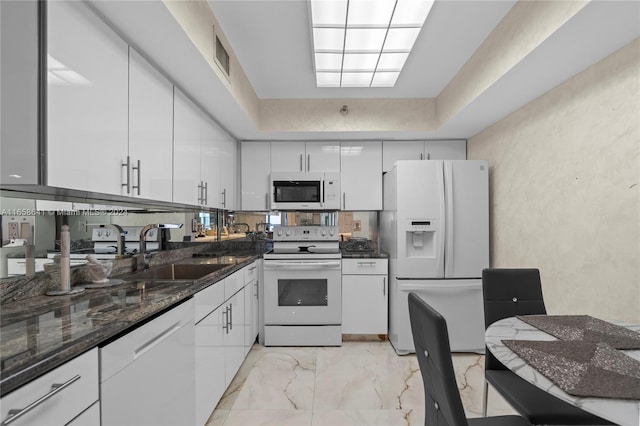 kitchen with white appliances, white cabinetry, sink, and dark stone countertops