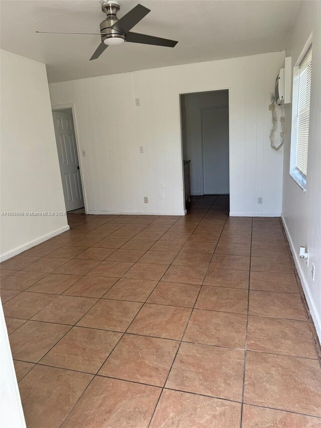 unfurnished room with tile patterned flooring, wood walls, and ceiling fan