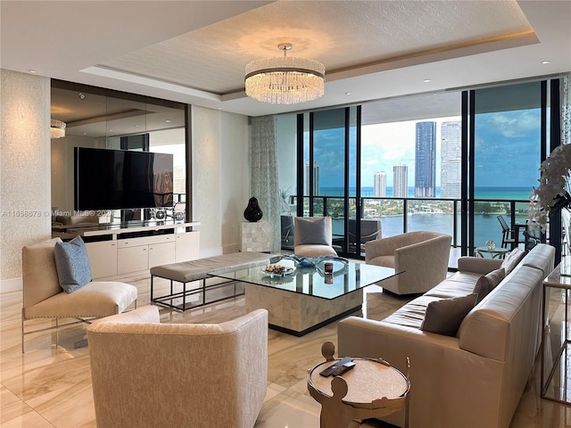 tiled living room featuring a water view, a wall of windows, a textured ceiling, an inviting chandelier, and a tray ceiling