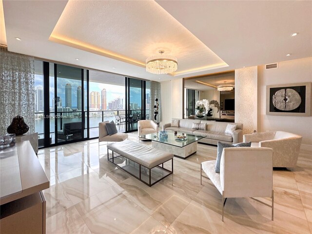 living area featuring a tray ceiling, visible vents, floor to ceiling windows, and an inviting chandelier