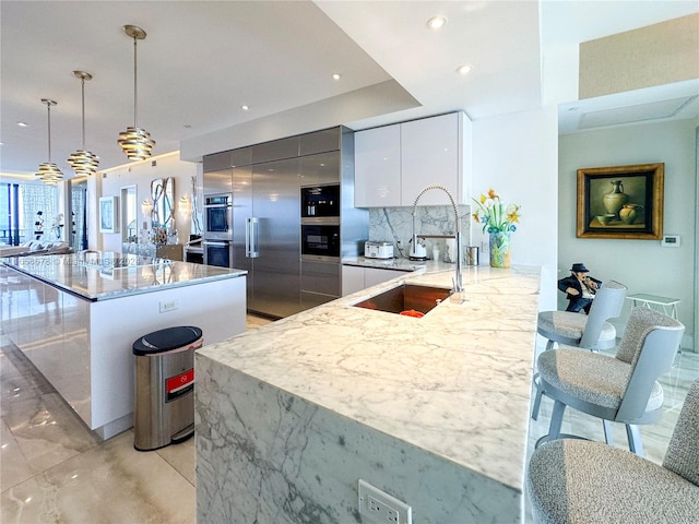 kitchen with modern cabinets, a sink, backsplash, white cabinets, and light stone countertops