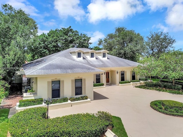 view of front facade featuring stucco siding, roof with shingles, and curved driveway