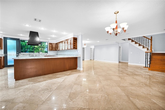 kitchen with wall chimney exhaust hood, pendant lighting, tasteful backsplash, kitchen peninsula, and light stone counters