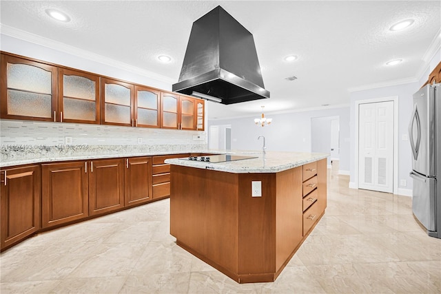 kitchen featuring a kitchen island with sink, stainless steel fridge, tasteful backsplash, hanging light fixtures, and island exhaust hood