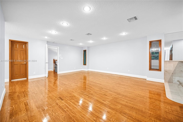 unfurnished living room featuring baseboards, a textured ceiling, visible vents, and light wood-style floors