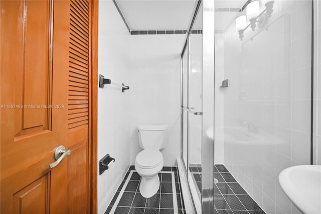 bathroom featuring tile patterned flooring, a shower with shower door, toilet, and tile walls