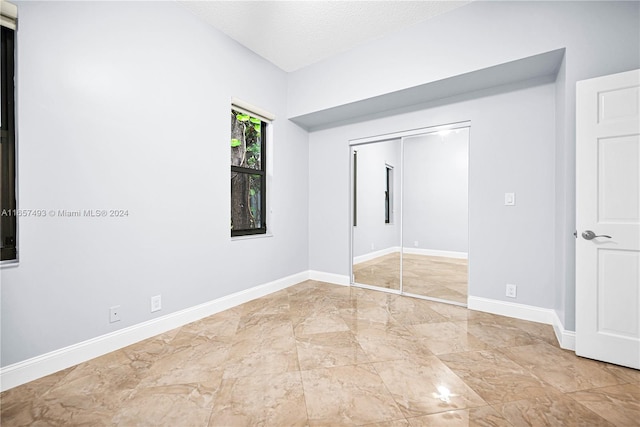 unfurnished bedroom with marble finish floor, baseboards, a textured ceiling, and a closet