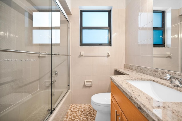 full bath with toilet, tile walls, tile patterned flooring, vanity, and enclosed tub / shower combo
