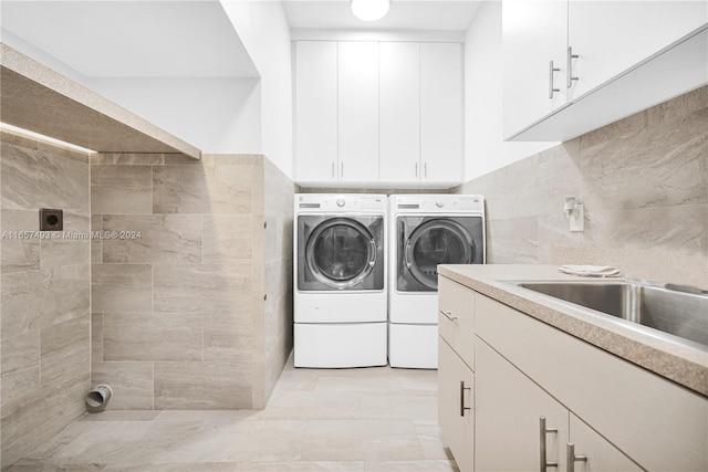 clothes washing area featuring washing machine and dryer, a sink, and tile walls