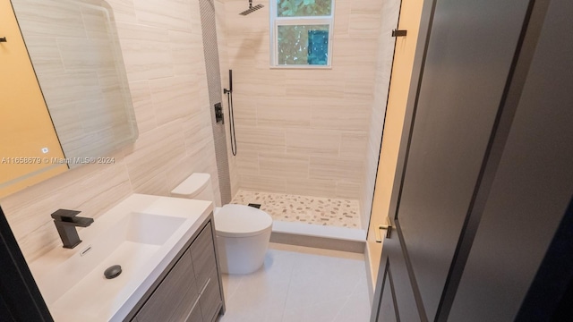 bathroom with toilet, tile patterned flooring, vanity, a tile shower, and tile walls