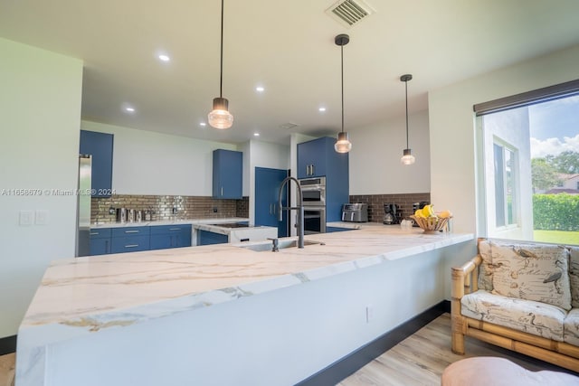 kitchen featuring light wood-type flooring, appliances with stainless steel finishes, kitchen peninsula, blue cabinets, and tasteful backsplash