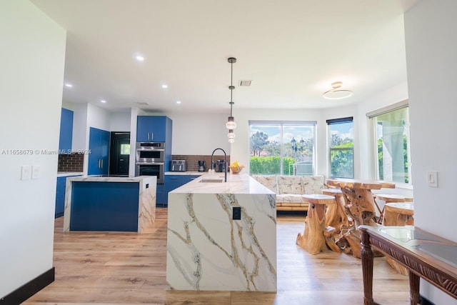 kitchen with pendant lighting, light hardwood / wood-style floors, blue cabinetry, and tasteful backsplash