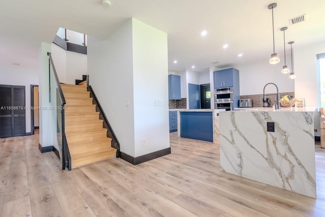 kitchen with light hardwood / wood-style flooring, a kitchen island, stainless steel double oven, and blue cabinetry