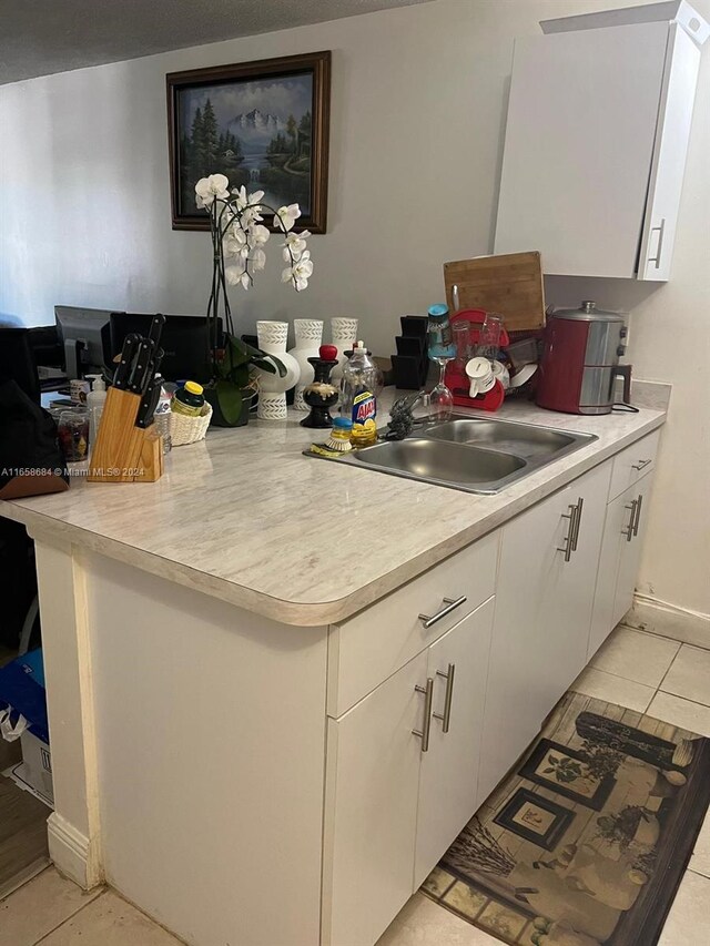 kitchen with light tile patterned floors, white cabinetry, and sink