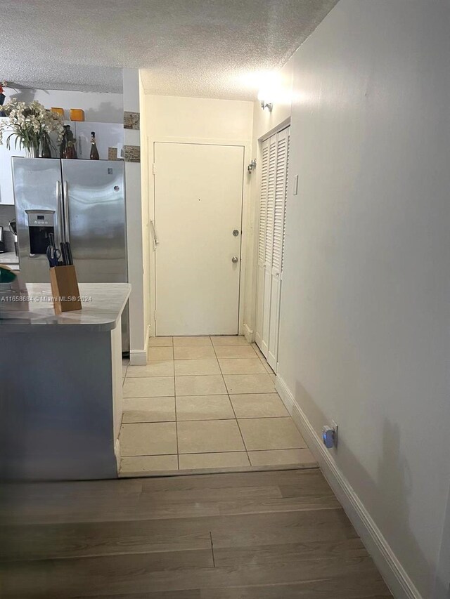 kitchen with a textured ceiling, light wood-type flooring, and stainless steel refrigerator with ice dispenser