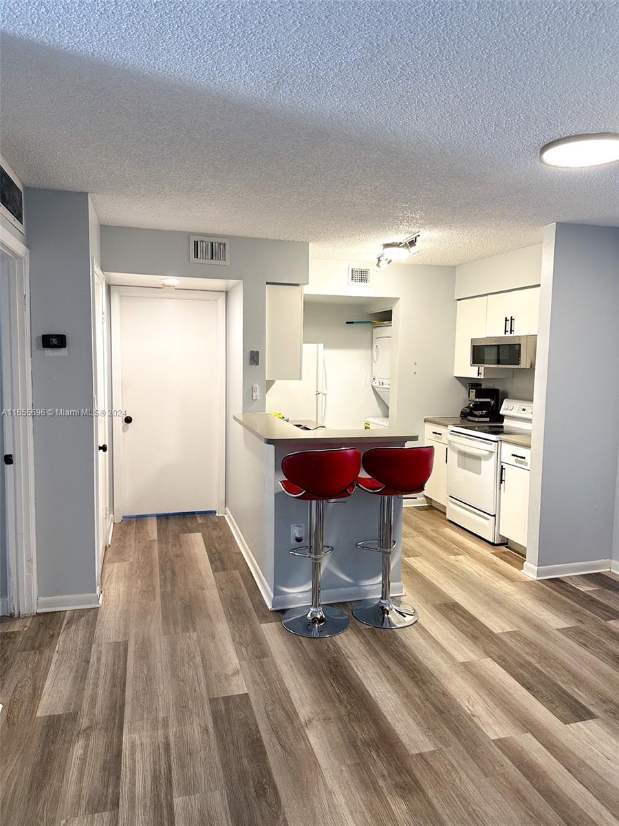 kitchen featuring a textured ceiling, white appliances, white cabinets, and light hardwood / wood-style floors