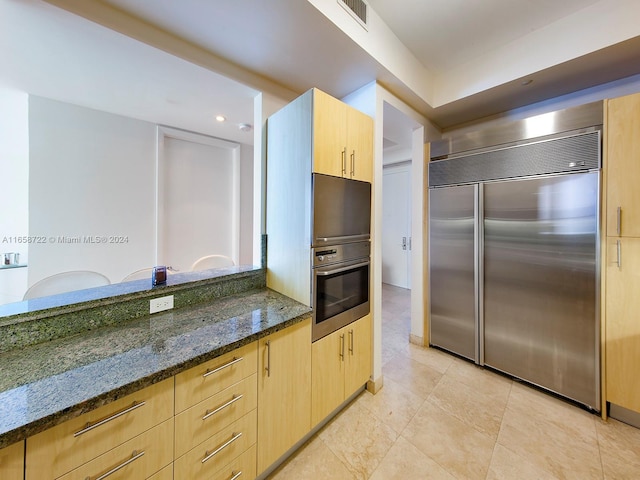 kitchen with stainless steel appliances, dark stone counters, and light brown cabinetry