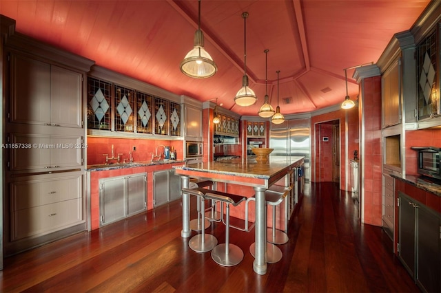 kitchen featuring hanging light fixtures, a center island, light stone counters, dark hardwood / wood-style flooring, and a kitchen bar