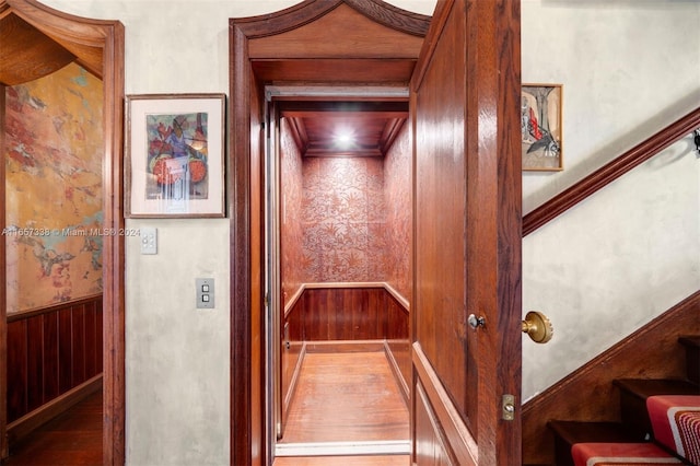 interior space featuring wood-type flooring, wooden walls, and elevator