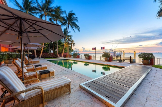 pool at dusk with a water view and a patio