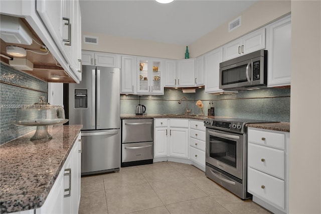 kitchen with appliances with stainless steel finishes, dark stone countertops, backsplash, and white cabinetry