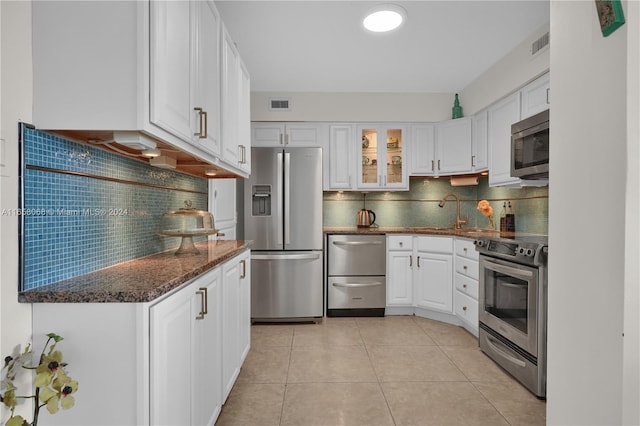 kitchen with white cabinets, light tile patterned floors, stainless steel appliances, dark stone counters, and tasteful backsplash