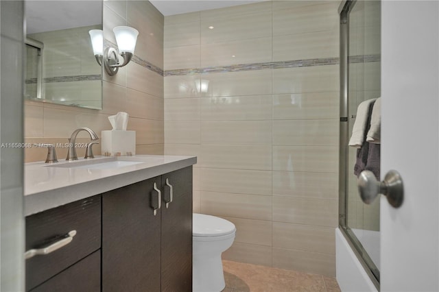 full bathroom featuring toilet, tile patterned floors, vanity, enclosed tub / shower combo, and tile walls