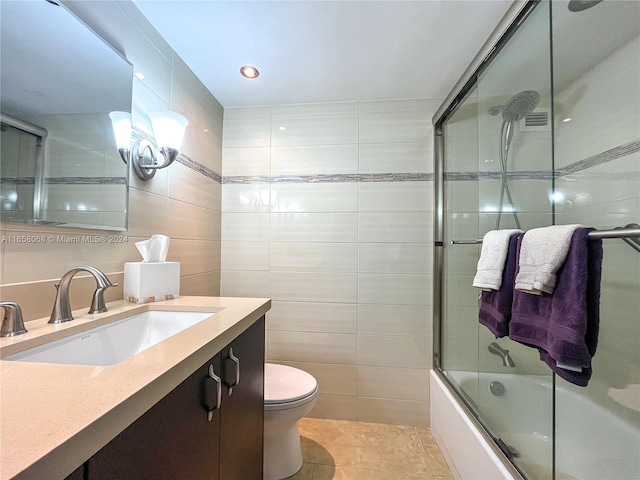 full bathroom featuring toilet, tile patterned flooring, vanity, enclosed tub / shower combo, and tile walls