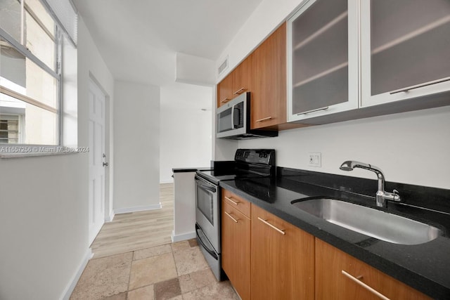 kitchen featuring appliances with stainless steel finishes, dark stone countertops, sink, and light hardwood / wood-style flooring