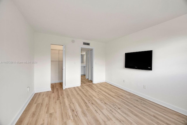 unfurnished bedroom with light wood-type flooring, a closet, and a walk in closet