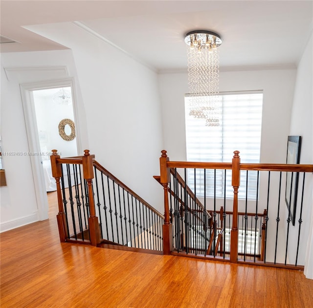 stairway featuring wood-type flooring, an inviting chandelier, and ornamental molding