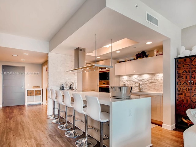 kitchen featuring tasteful backsplash, light hardwood / wood-style flooring, a kitchen bar, kitchen peninsula, and wall oven