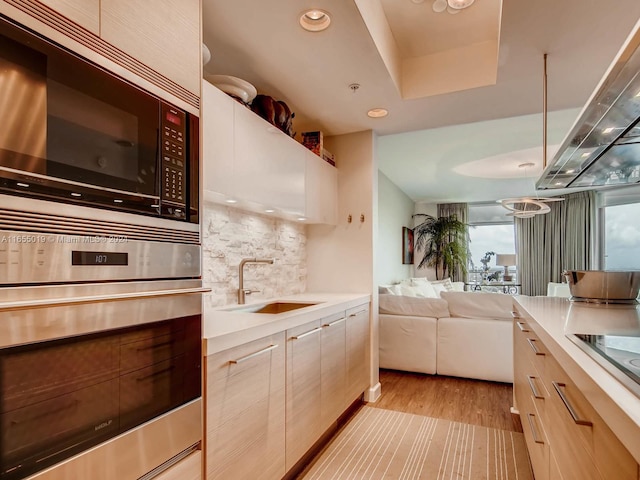 kitchen with exhaust hood, black appliances, light hardwood / wood-style flooring, sink, and decorative backsplash