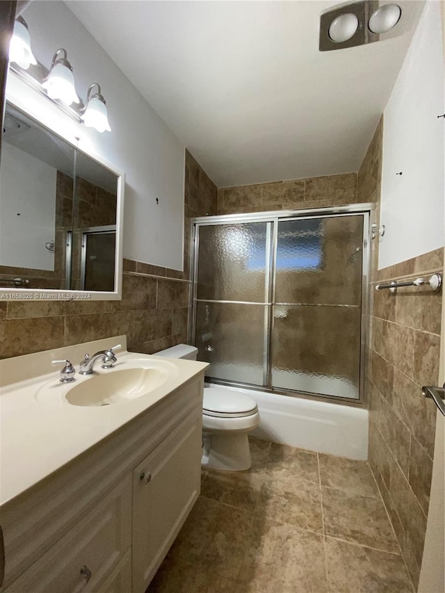 full bathroom featuring toilet, tile patterned flooring, shower / bath combination with glass door, vanity, and tile walls