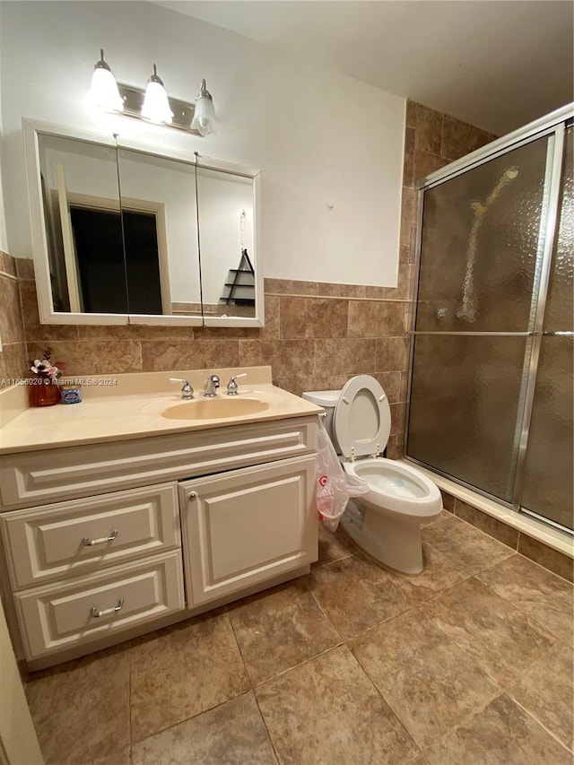 bathroom featuring tile patterned flooring, a shower with door, toilet, tile walls, and vanity