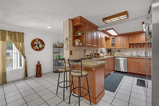 kitchen with a textured ceiling, a breakfast bar area, light stone countertops, dishwasher, and kitchen peninsula