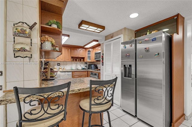 kitchen with light tile patterned floors, a breakfast bar, stainless steel appliances, sink, and kitchen peninsula