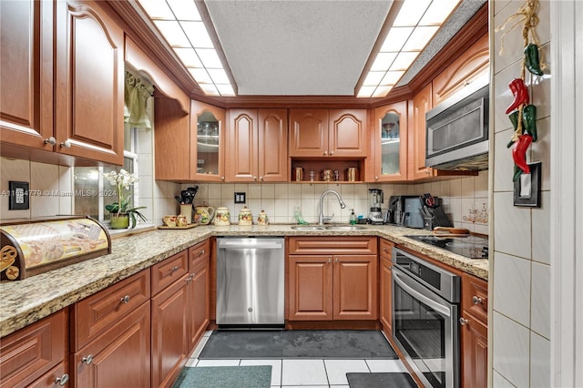 kitchen with dark tile patterned flooring, light stone counters, sink, decorative backsplash, and appliances with stainless steel finishes