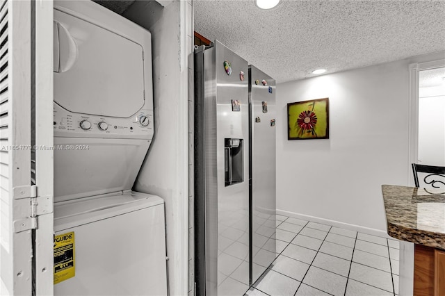 clothes washing area featuring light tile patterned floors, stacked washing maching and dryer, and a textured ceiling