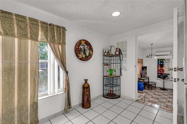 interior space with a wall mounted AC, light tile patterned floors, a textured ceiling, and an inviting chandelier