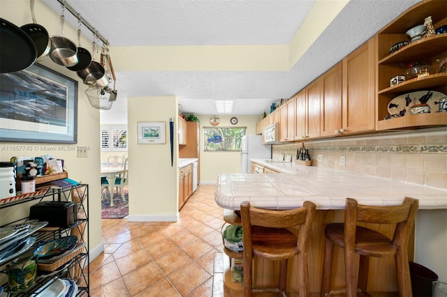 kitchen featuring backsplash, white appliances, kitchen peninsula, a kitchen bar, and tile counters