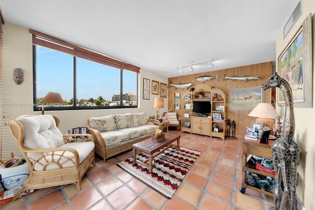 living room with rail lighting, tile patterned floors, and wooden walls