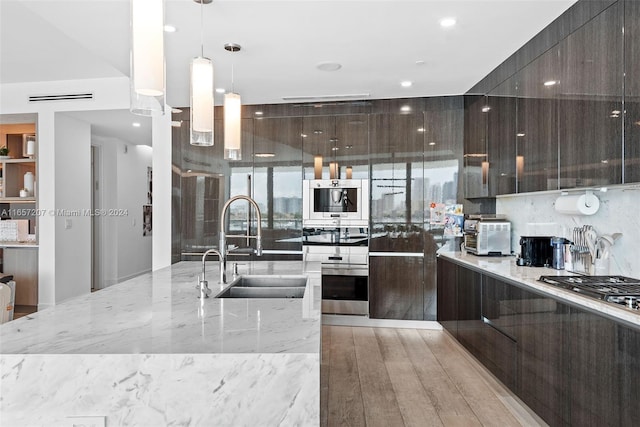 kitchen with light stone countertops, hanging light fixtures, stainless steel appliances, sink, and light wood-type flooring