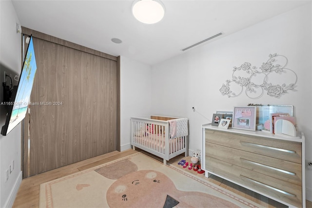 bedroom with light wood-type flooring and a nursery area